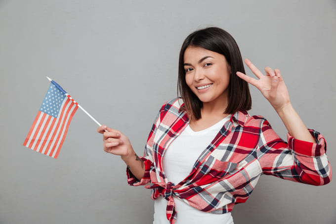 mulher sorrindo com a bandeira dos estados unidos na mao e fazendo dois nos dedos