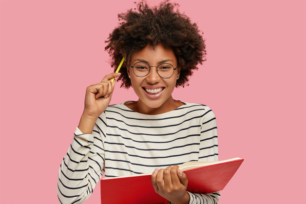 mulher sorrindo com caneta na cabeça e caderno na mao